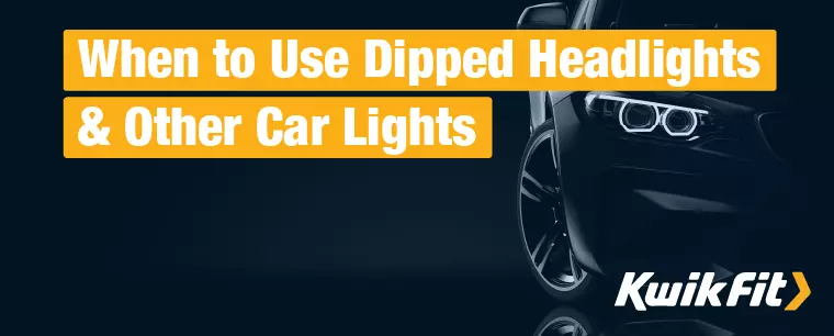 A sleek, modern black car in a dark space with only the trim edges and the headlight lit up.